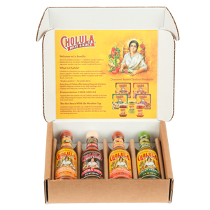 A cardboard gift box displays four different flavors of Cholula Hot Sauce: Chili Garlic, Extra Hot, Sweet Habanero, and Green Pepper.