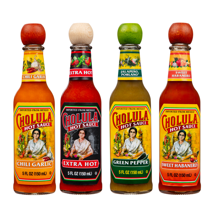 Four bottles of Cholula Hot Sauce are lined up against a black background, showcasing the Chili Garlic, Extra Hot, Green Pepper, and Sweet Habanero varieties.