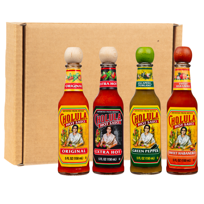 Four bottles of Cholula Hot Sauce in Original, Extra Hot, Green Pepper, and Sweet Habanero flavors are lined up in front of a cardboard box.