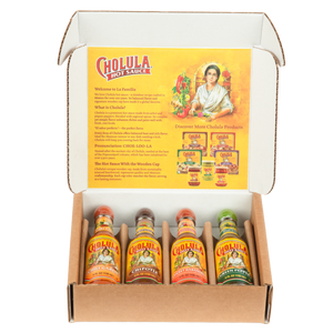 An open gift box displays a Cholula Hot Sauce Variety Pack, featuring Chili Garlic, Chipotle, Sweet Habanero, and Green Pepper flavors, with an informational insert about the brand's history.