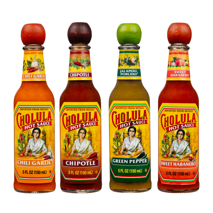 Four bottles of Cholula Hot Sauce are lined up against a black background, showcasing the Chili Garlic, Chipotle, Green Pepper, and Sweet Habanero flavors.