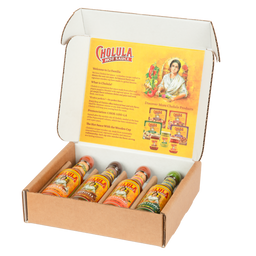 A Cholula hot sauce variety pack is displayed in an open cardboard box, showing four different flavors with their signature wooden caps.