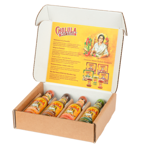 A Cholula hot sauce variety pack is displayed in an open cardboard box, showing four different flavors with their signature wooden caps.