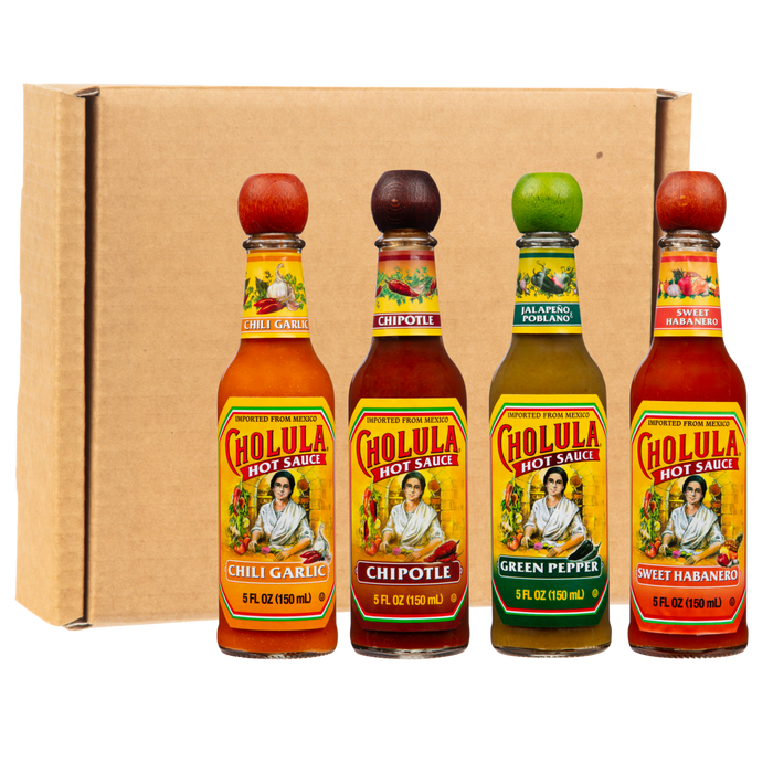 Four bottles of Cholula Hot Sauce in the flavors Chili Garlic, Chipotle, Green Pepper, and Sweet Habanero are arranged in a row in front of a cardboard box.