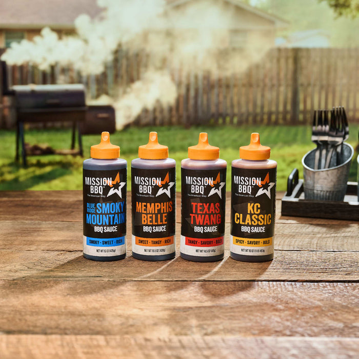 Four different bottles of barbecue sauce from the Mission Bbq Iw Dtc Pack Bundle Dtcmbbqvp are lined up on a wooden picnic table with a smoking grill in the background.