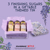 This image shows a giftable themed tin containing three jars of McCormick Bridgerton Finishing Sugars, including Sweet Lemon, Strawberries &amp; Cream, and Lavender Vanilla.