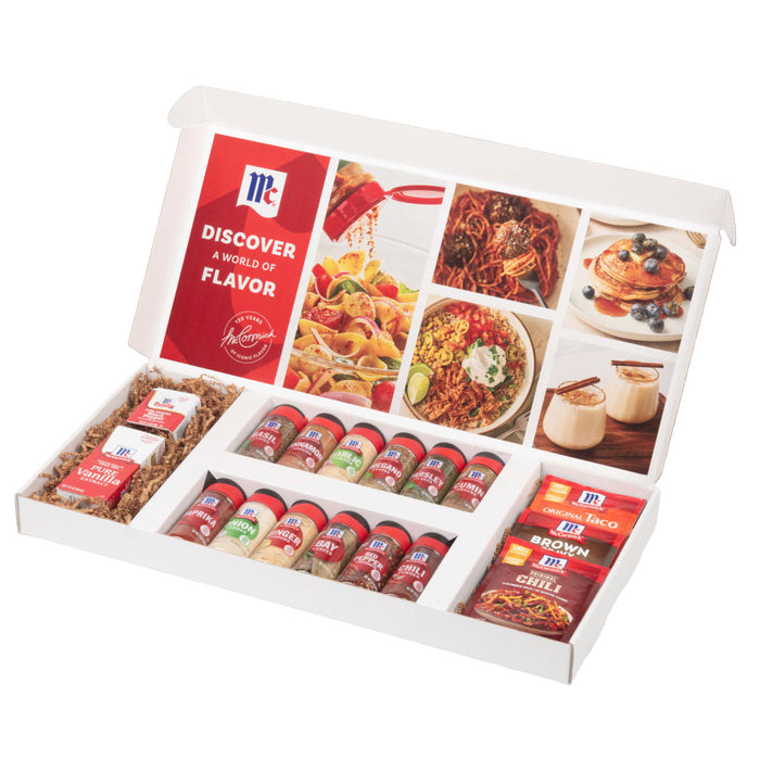 A McCormick Discover a World of Flavor gift set is displayed open, showcasing a variety of spices like Basil and Paprika, seasoning packets for Taco and Chili, and Pure Vanilla Extract, all arranged in a white box.