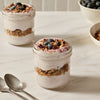 Two glass jars are filled with yogurt and granola parfaits, topped with fresh blueberries and a sprinkle of Mccormick Blueberry And Lemon Finishing Sugar, 3.43 Oz.