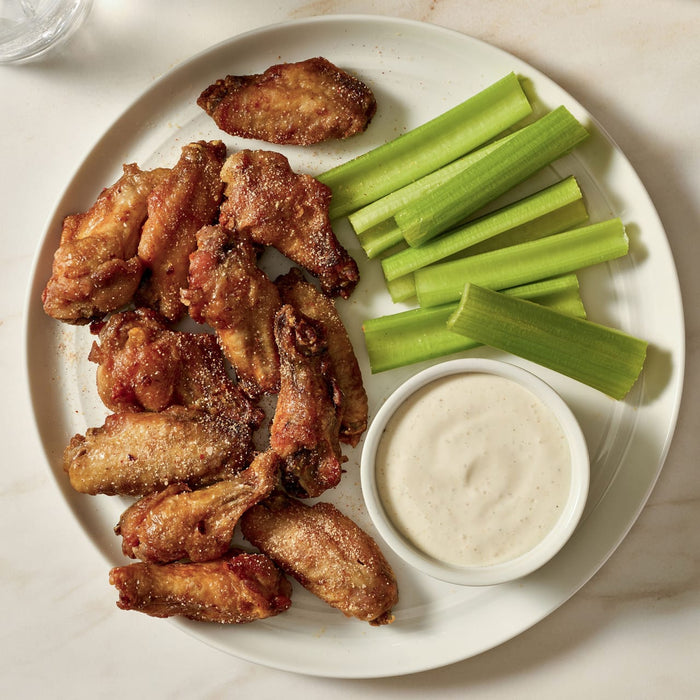 A plate of chicken wings seasoned with Mccormick Honey Chipotle Finishing Salt, 3.07 Oz, is served with celery sticks and a creamy dipping sauce.