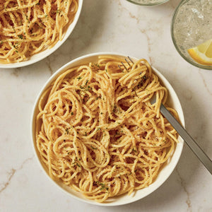 A top-down view shows a white bowl of spaghetti topped with a generous amount of Mccormick Zesty Lemon Finishing Salt, 4.97 Oz and chopped parsley, with a fork resting in the pasta.