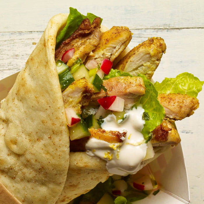 A close-up of a chicken shawarma wrap with lettuce cucumber radish and a creamy sauce.