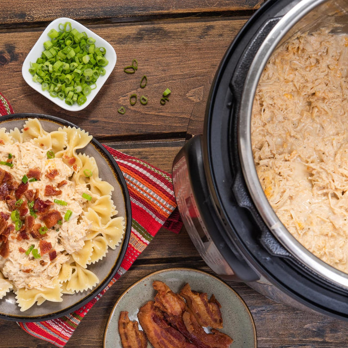 A plate of pasta with chicken bacon and green onions a plate of bacon and a pressure cooker with chicken in it.