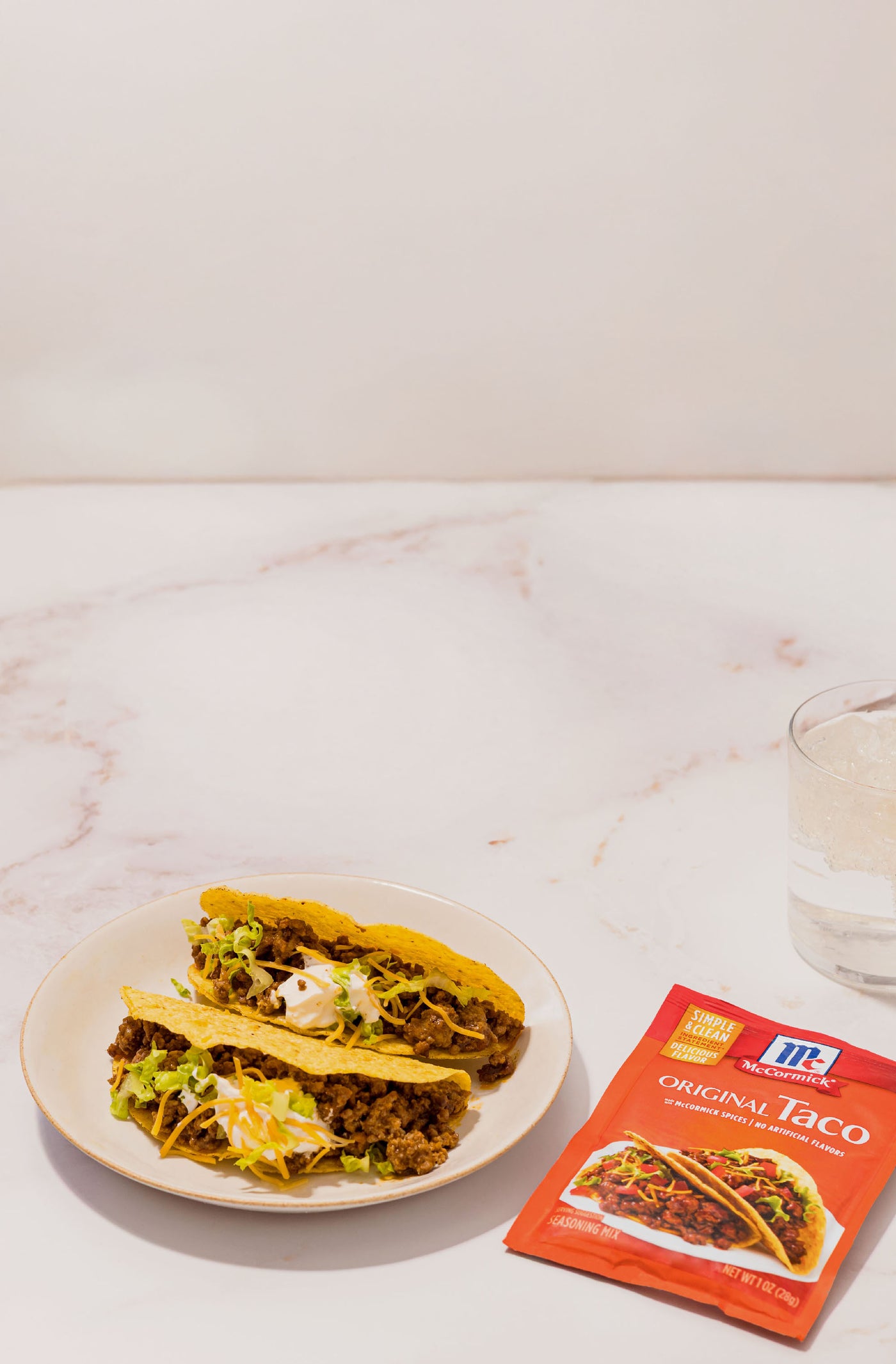 Two tacos on a plate with a McCormick original taco seasoning on a marble surface.