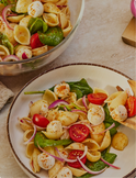 Pasta salad with tomatoes, onions, and greens on a plate