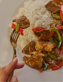 Plated dish of stir-fried meat with vegetables over white rice, held with a fork.