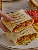 Hand holding a half burrito with visible ingredients on a plate, accompanied by a bowl of salsa.