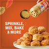 A hand sprinkles McCormick Pumpkin Pie Spice onto a stack of baked goods, highlighting its versatility for sprinkling, mixing, baking, and more.