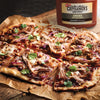 A pizza topped with pulled pork red onion cilantro peanuts and Cattlemens BBQ sauce.