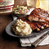 A plate of BBQ ribs with mashed potatoes and coleslaw with a bottle of Cattlemens BBQ sauce in the background.