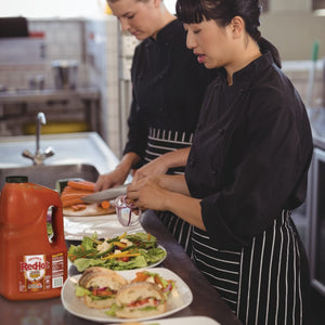 Two women in black chef uniforms prepare a meal with Franks RedHot Buffalo Sandwich Sauce.
