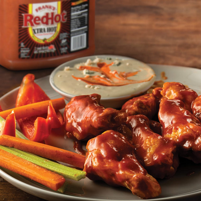 A plate of RedHot chicken wings with carrots celery and a side of blue cheese dressing.