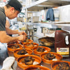 A chef is plating a dish of meat and sauce in a restaurant kitchen with a bottle of Frenchs Cattlemens BBQ Sauce in the foreground.