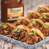 A close-up of pulled pork sliders topped with pickles and Cattlemens BBQ sauce.