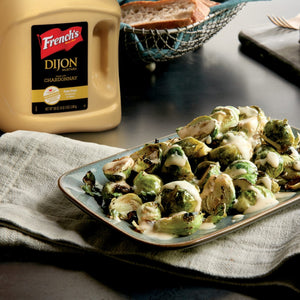A bottle of Frenchs Dijon Mustard next to a plate of roasted brussels sprouts with a creamy sauce.