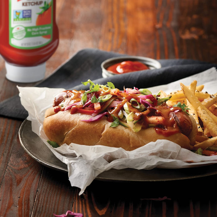 A hot dog with ketchup mustard and relish on a bun with french fries on the side.