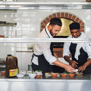 Two chefs in a kitchen preparing food with a bottle of Franks RedHot.