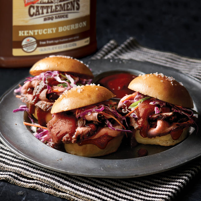 Three mini beef sandwiches with red cabbage slaw and Cattlemens BBQ sauce on a silver plate.