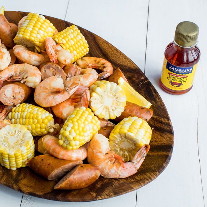 A wooden bowl filled with shrimp corn on the cob sausage and a bottle of Zatarains Shrimp &amp; Crab Boil.