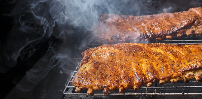 Barbecued ribs on a grill with smoke rising