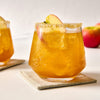 A festive apple cider cocktail with a sugared rim and apple slice garnish sits on a coaster.