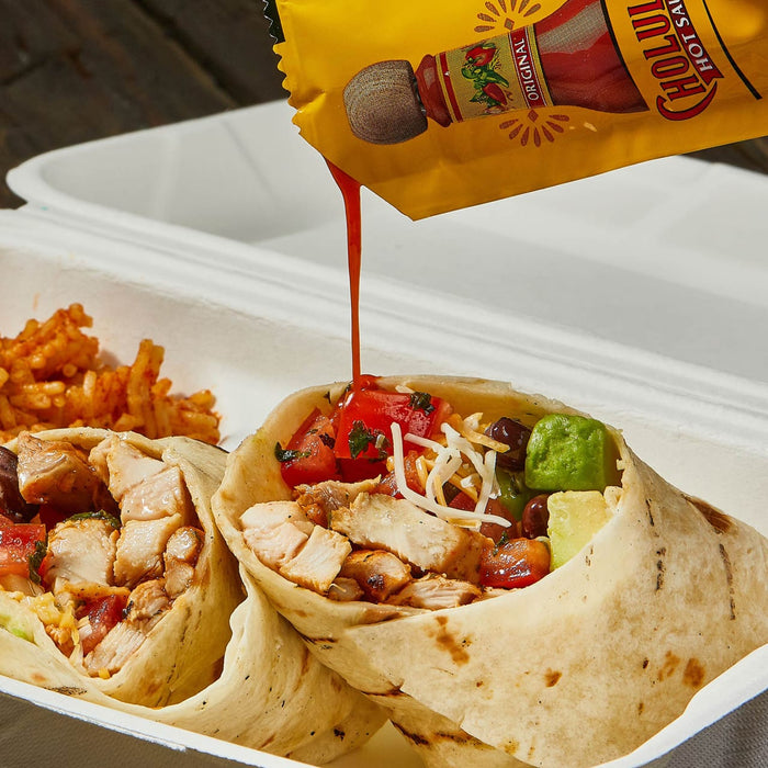 A close-up of a Cholula Hot Sauce packet being squeezed over a chicken burrito.