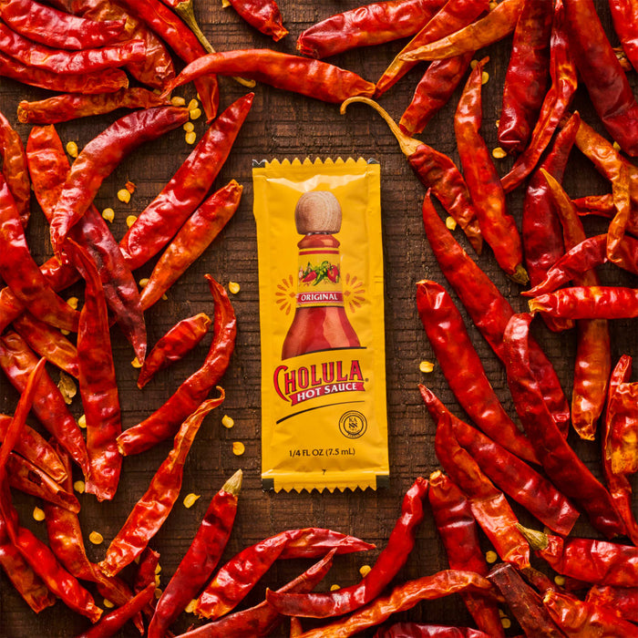 A packet of Cholula Original Hot Sauce surrounded by dried red chili peppers.