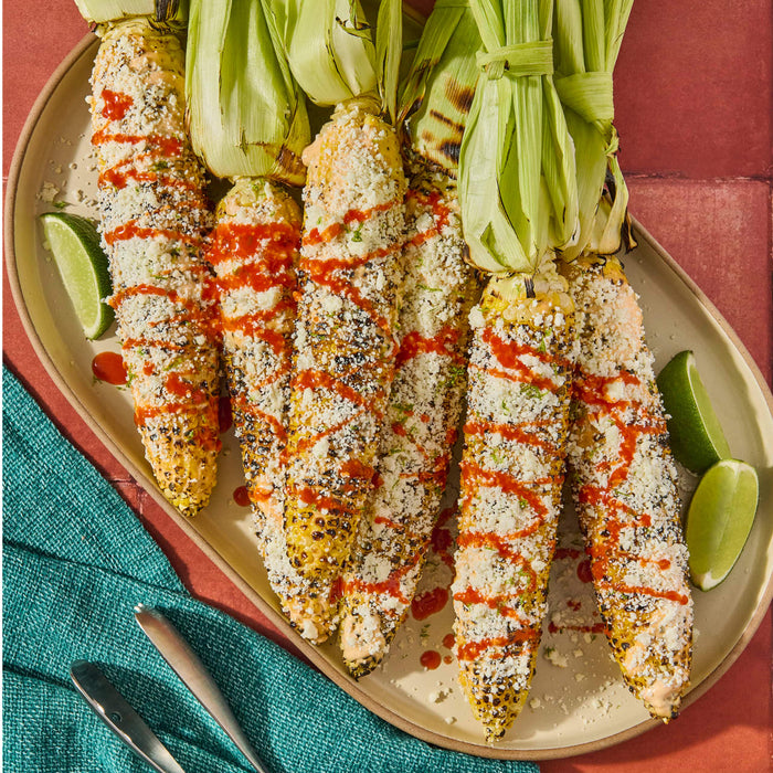Grilled corn on the cob topped with cotija cheese chili powder and lime wedges.