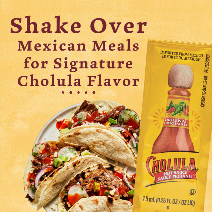 A plate of tacos topped with Cholula hot sauce with a packet of Cholula hot sauce in the background.