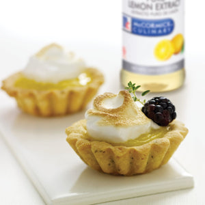 Two lemon tarts with meringue and a blackberry on top, with a bottle of McCormick Culinary Lemon Extract in the background.