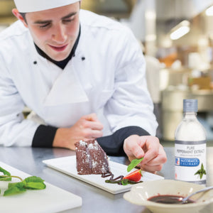 A chef is plating a chocolate cake with a strawberry and mint garnish, using McCormick Culinary Pure Peppermint Extract.