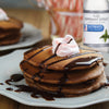 A plate of chocolate pancakes topped with whipped cream and chocolate sauce, with a bottle of McCormick Culinary Pure Peppermint Extract in the background.