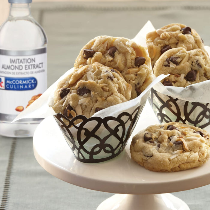 A bottle of McCormick Culinary Imitation Almond Extract next to a plate of chocolate chip cookies with coconut and almonds.