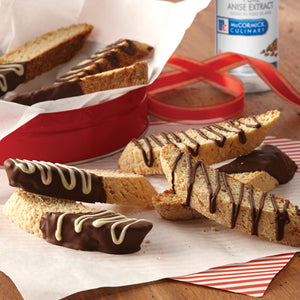 Biscotti dipped in chocolate and drizzled with white chocolate, next to a McCormick Culinary Anise Extract bottle.