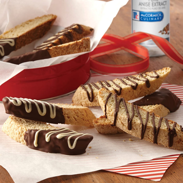 Biscotti dipped in chocolate and drizzled with white chocolate, next to a McCormick Culinary Anise Extract bottle.