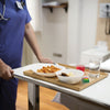A nurse is pushing a medical cart with a meal tray on it.