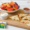 A close-up of a wooden cutting board with a bowl of tortilla chips, a bowl of sour cream, a bowl of salsa, and three quesadillas with a packet of McCormick Salt-Free Classic Blend seasoning.