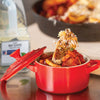 A red Le Creuset pot with a lid on top, filled with a tomato-based dish topped with a piece of toasted bread.