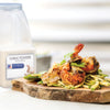 A wooden cutting board with a serving of grilled shrimp with zucchini noodles and a container of McCormick Garlic Powder.