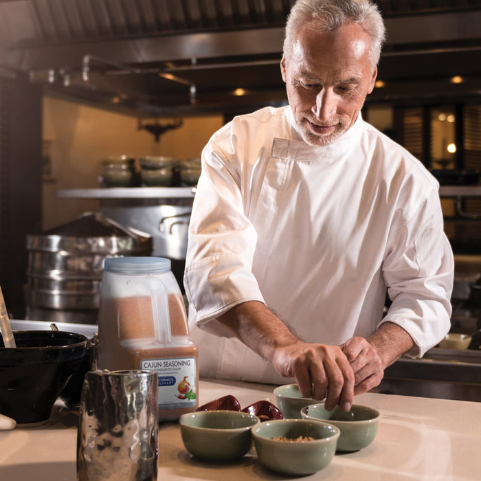 A chef in a white chefs coat is preparing food in a kitchen using McCormick Culinary Cajun Seasoning.