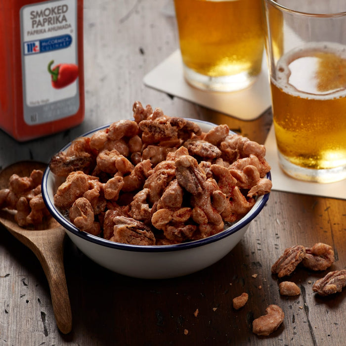 A bowl of McCormick Culinary Smoked Paprika Cashews and Pecans with two glasses of beer in the background.